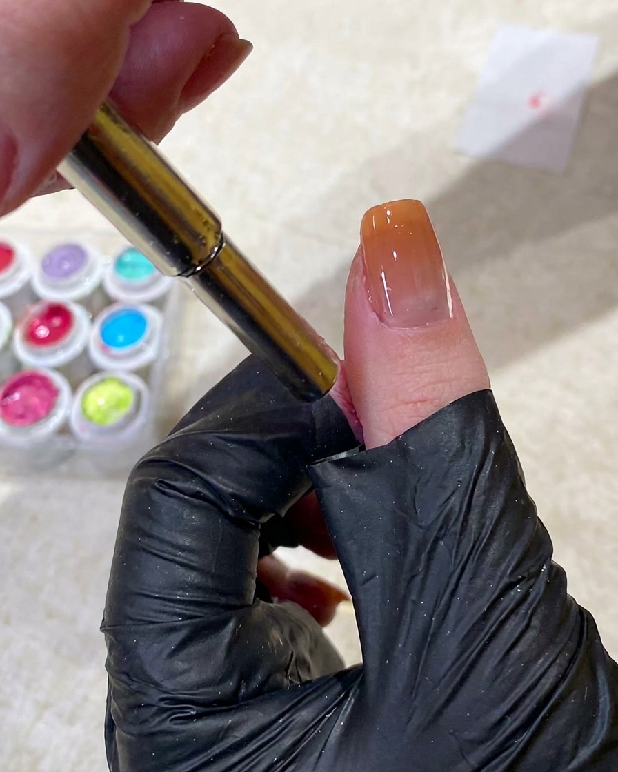 A magnet tool being used to manipulate cat-eye gel into a small circular bead shape near the cuticle.
