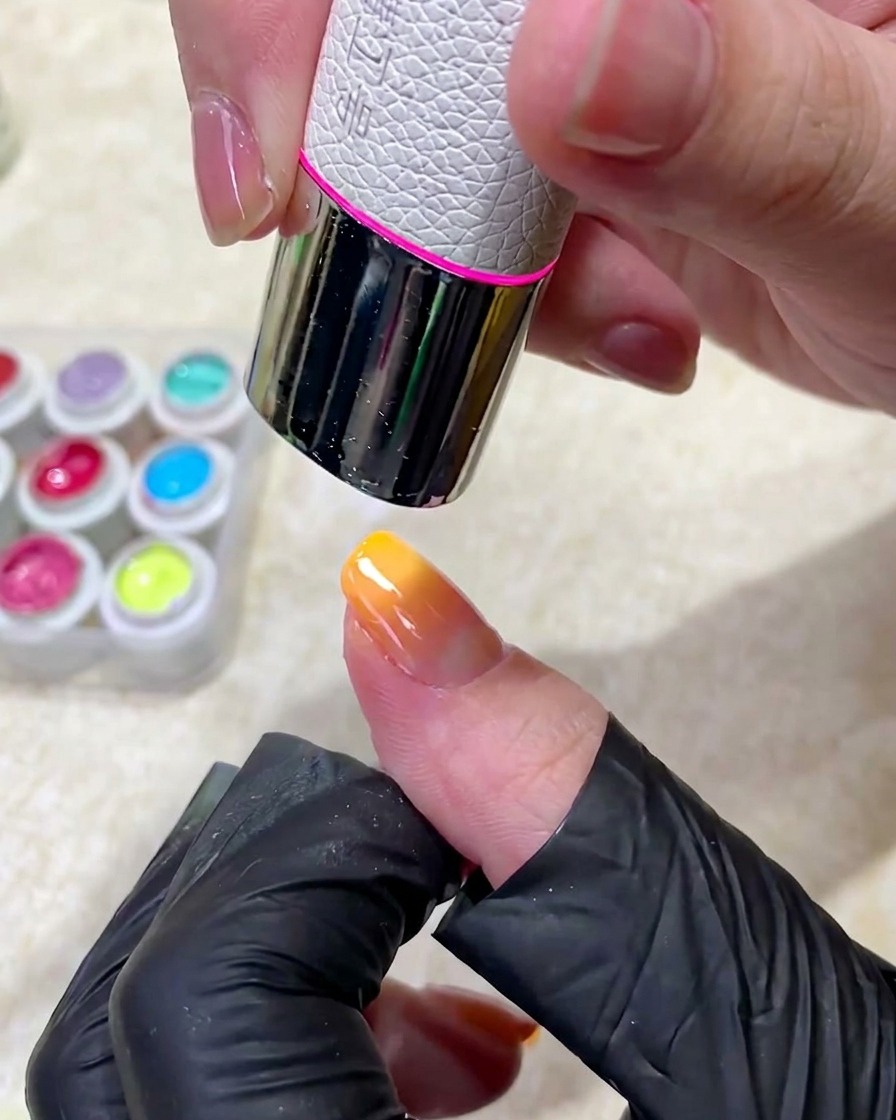 A manicured finger being placed under a professional UV nail lamp to cure the gel polish application.