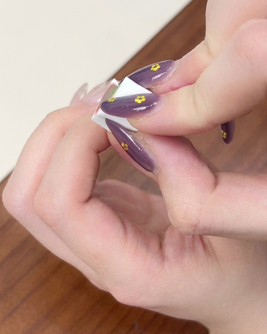 Fingers holding a small white makeup sponge, patting and blending blue gel polish into an ombre effect on a fingernail.