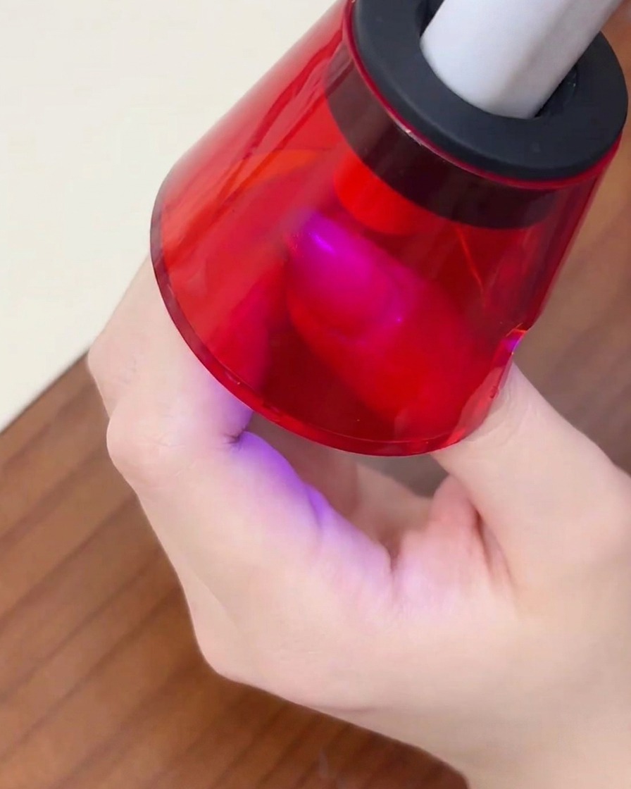 A finger resting under a mini red portable UV lamp to cure the gel polish.