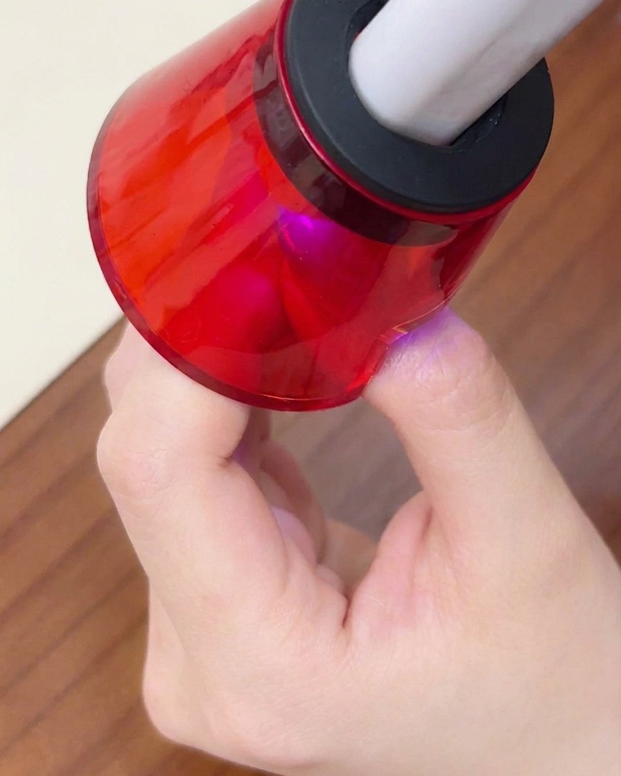 A close-up of a finger placed under a mini red portable UV/LED lamp for the final cure.