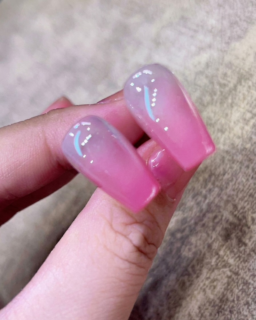 A close-up of a clear base coat being applied with a brush to a clean, natural nail.