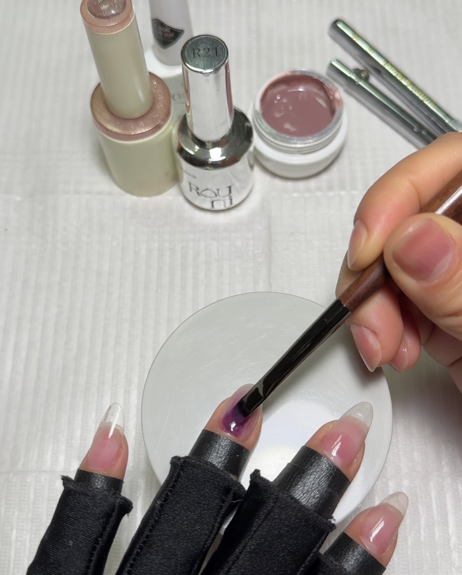A hand positioned inside a purple UV nail lamp with a nude-colored gel base coat on the nails.