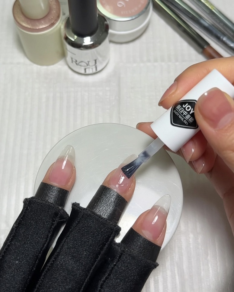 Applying milky white gel polish to the top half of a prepped pinkish-nude nail using the polish bottles brush.