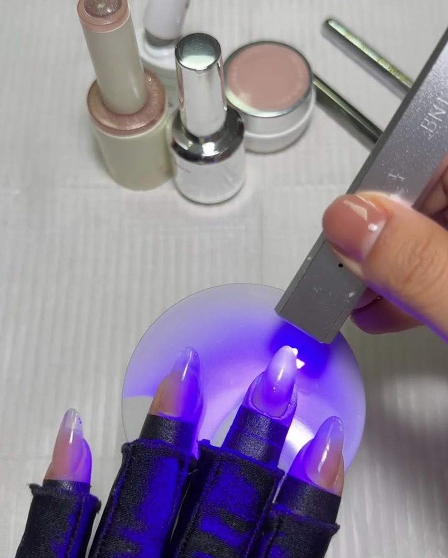 A hand with a gradient manicure placed inside a UV/LED lamp, curing under purple light.