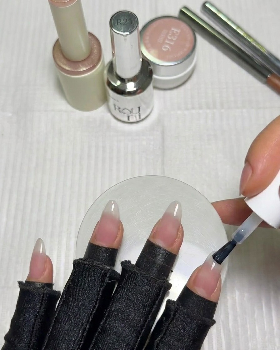 A nail brush applying a small amount of milky white gel polish to the tip of a nail.