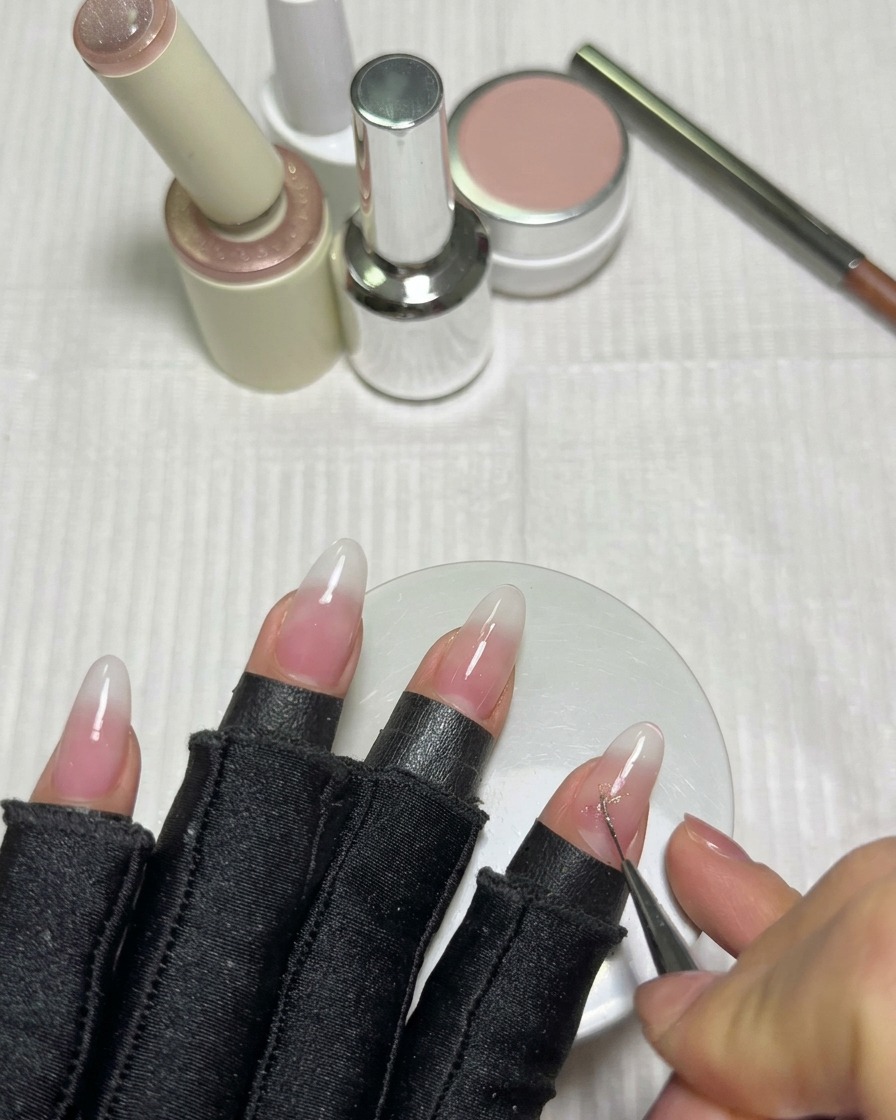 A fine liner brush drawing the intersecting lines of a star using pink cat-eye gel on a milky white nail.
