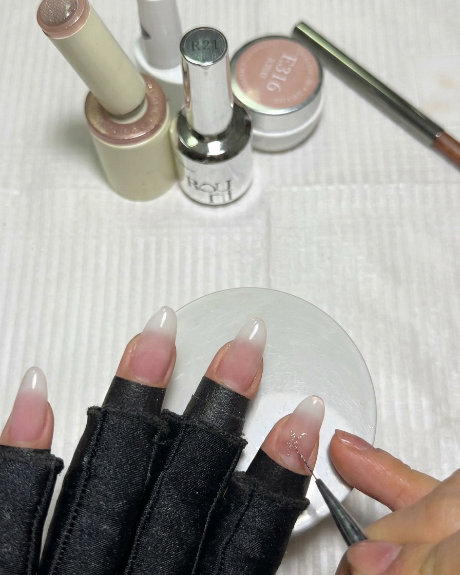 A fine liner brush filling in the center of a pink gel star on the nail to create sharp points.