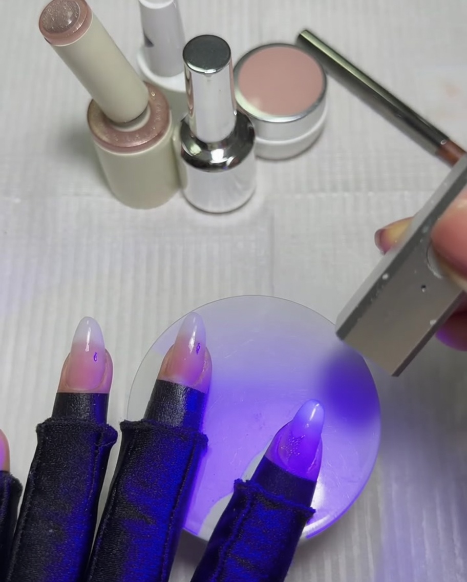 Nails resting under a purple UV and LED lamp to cure the freshly activated cat-eye star.