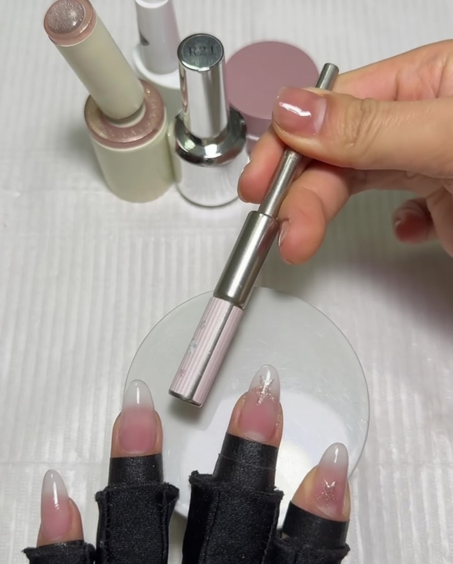 A cylindrical magnet being held horizontally over a thumb nail to activate the magnetic gel polish.
