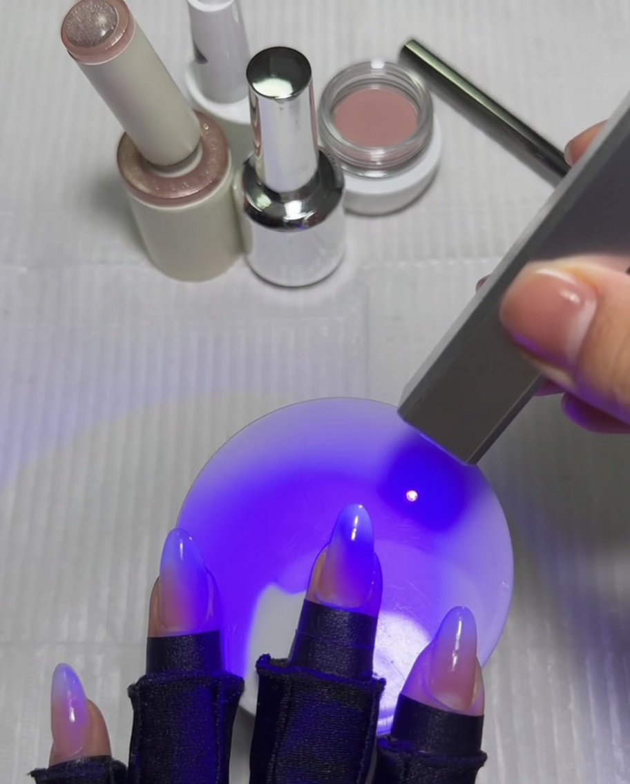 A hand with nails under a UV lamp, with the thumb being cured after the cat-eye star design is finished.