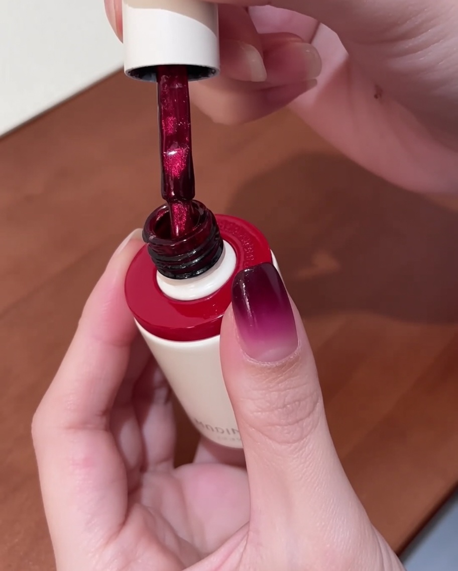 A brush applying vibrant red cat-eye gel polish onto a nail that already has a gradient base.