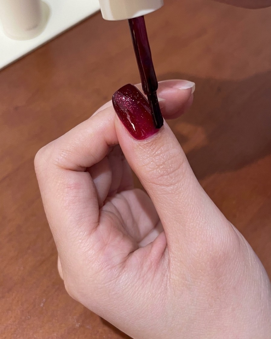 A magnetic tool held above a fingernail coated in wet red cat-eye gel, pulling the shimmer into a bright line.