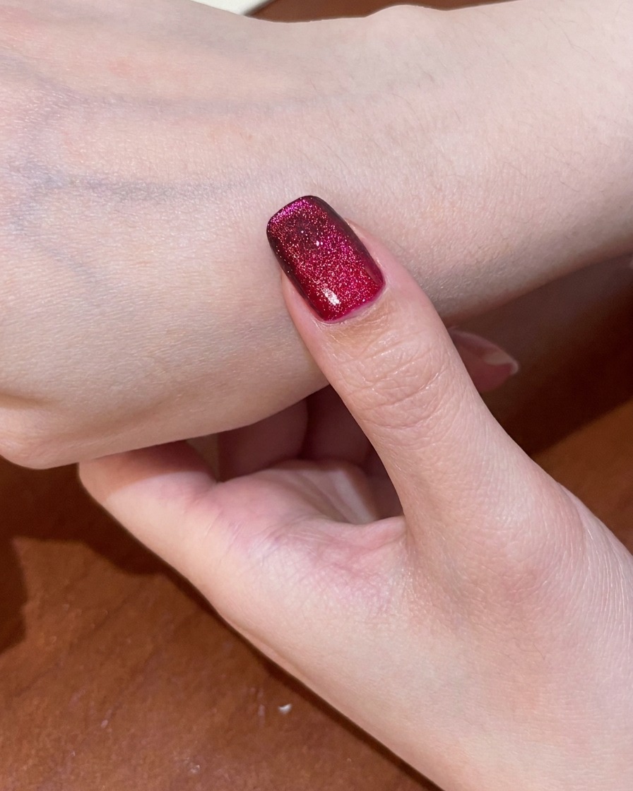 A fingernail with the completed red cat-eye design being cured inside a UV lamp.