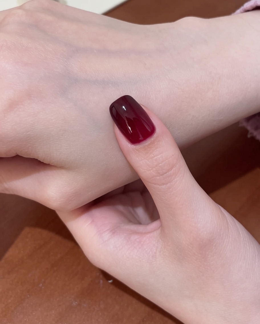 A brush applying a clear, glossy top coat over the finished red cat-eye nail design.