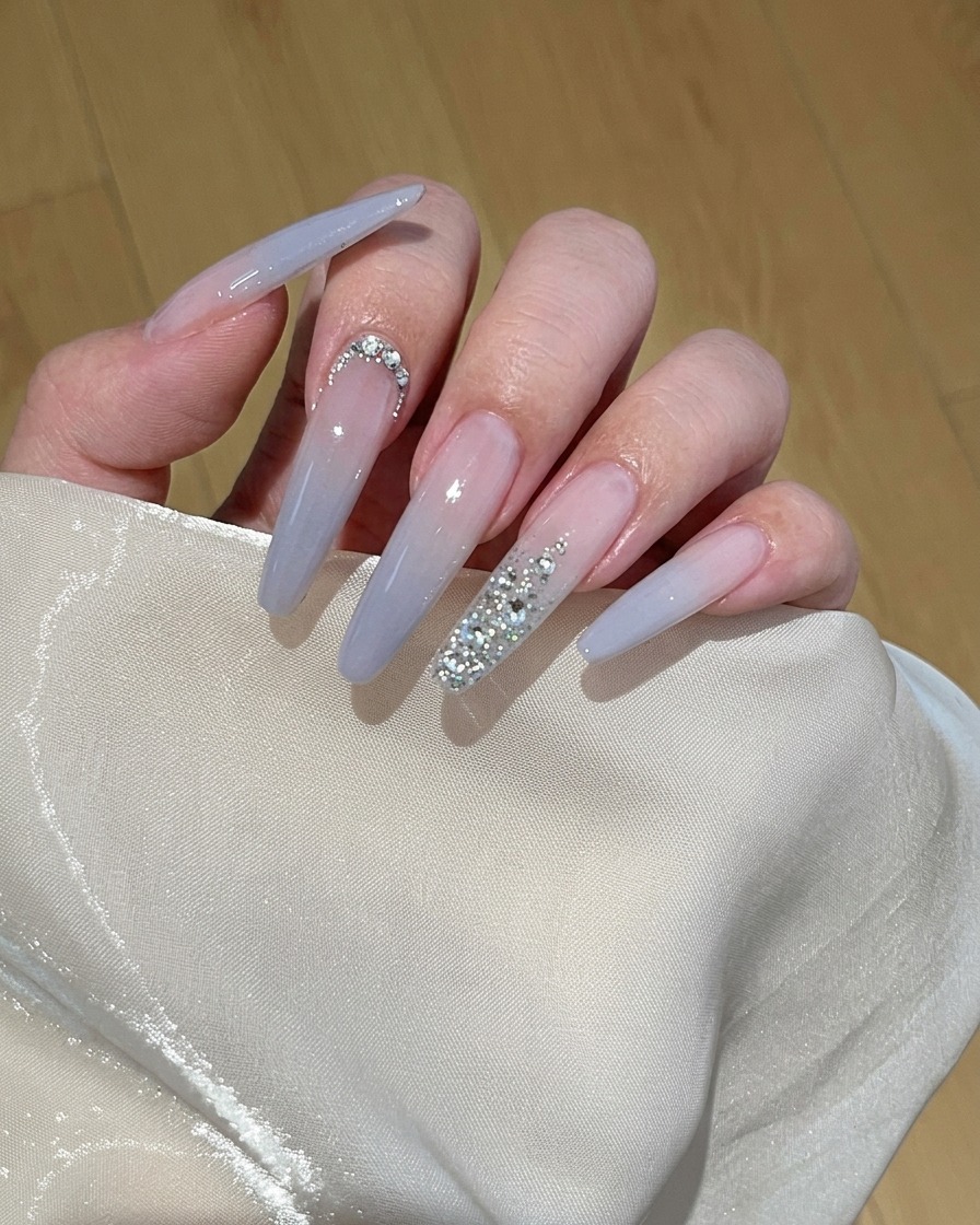 A close-up view of a brush applying light peach gel polish onto a natural fingernail.