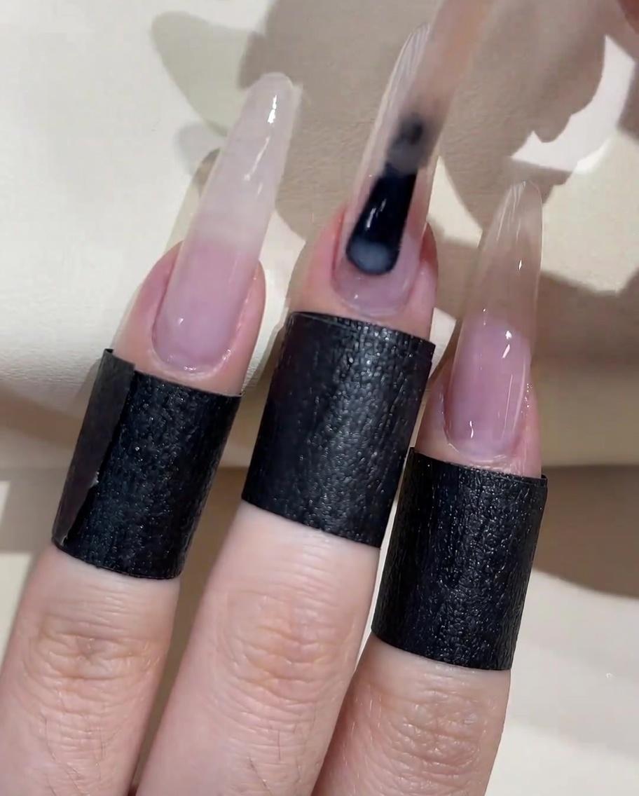 A brush applying a second coat of milky white peach gel polish over the nail surface.