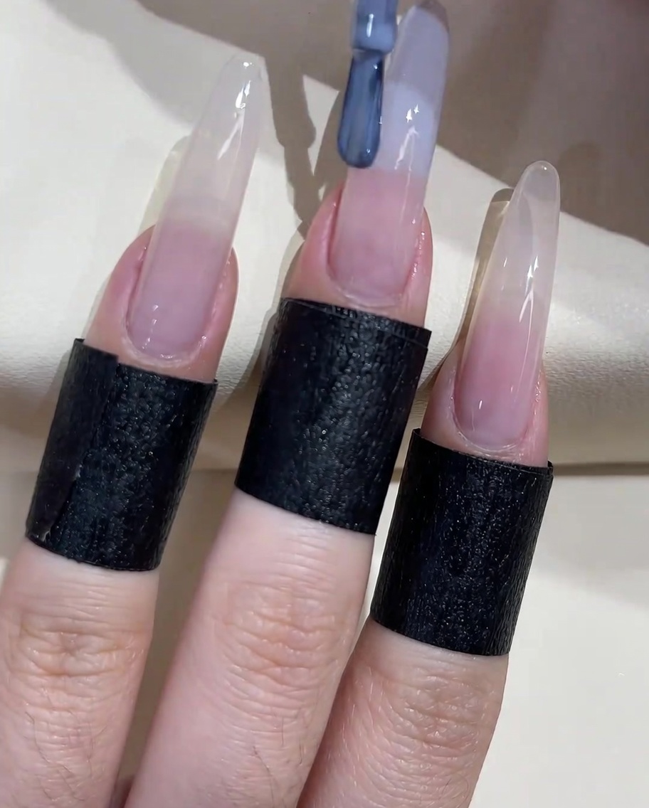 A nail brush applying a grey-blue gel polish to the free edge of the nail.