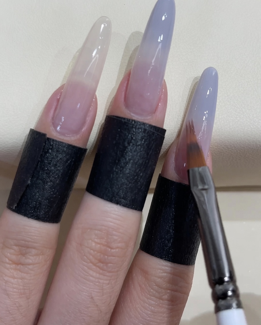 A small nail brush applying more grey-blue polish to the tip of the nail.