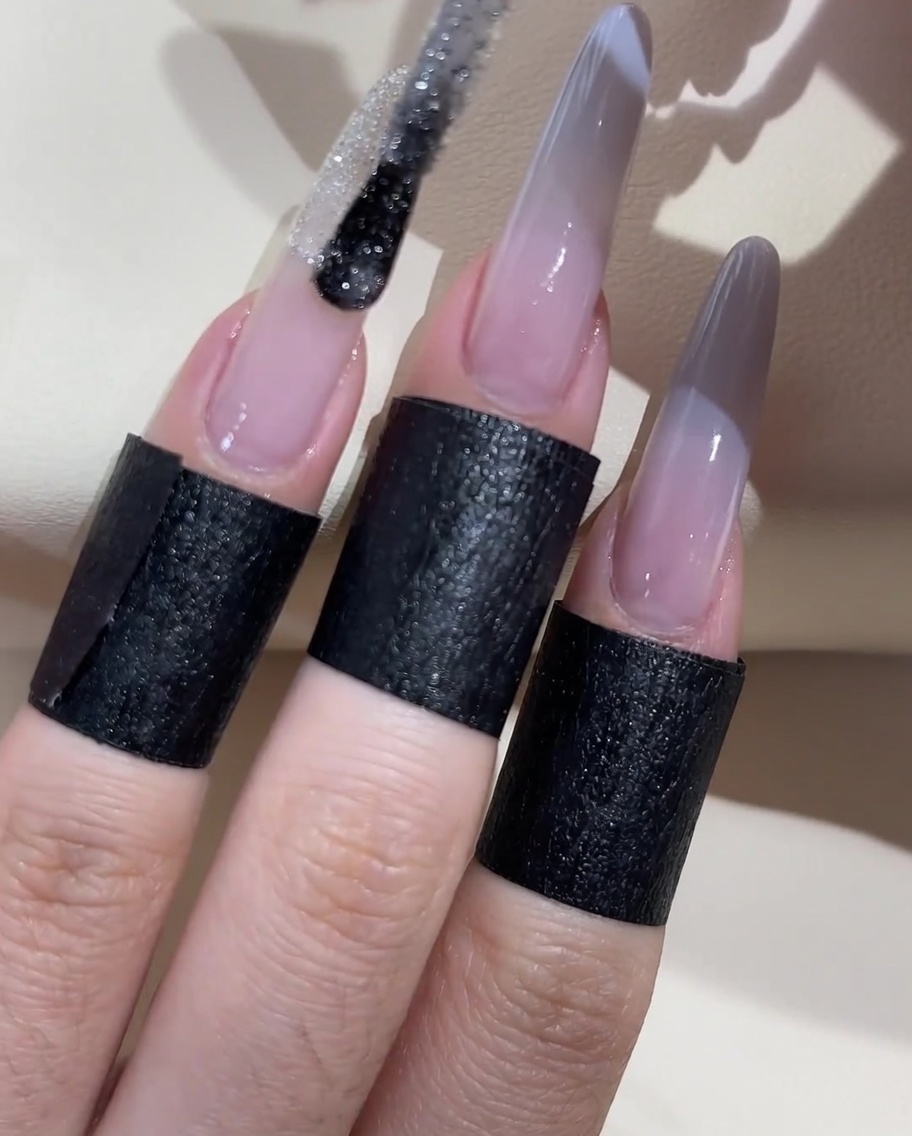 A brush applying a line of silver glitter polish across the middle of the ombre transition.