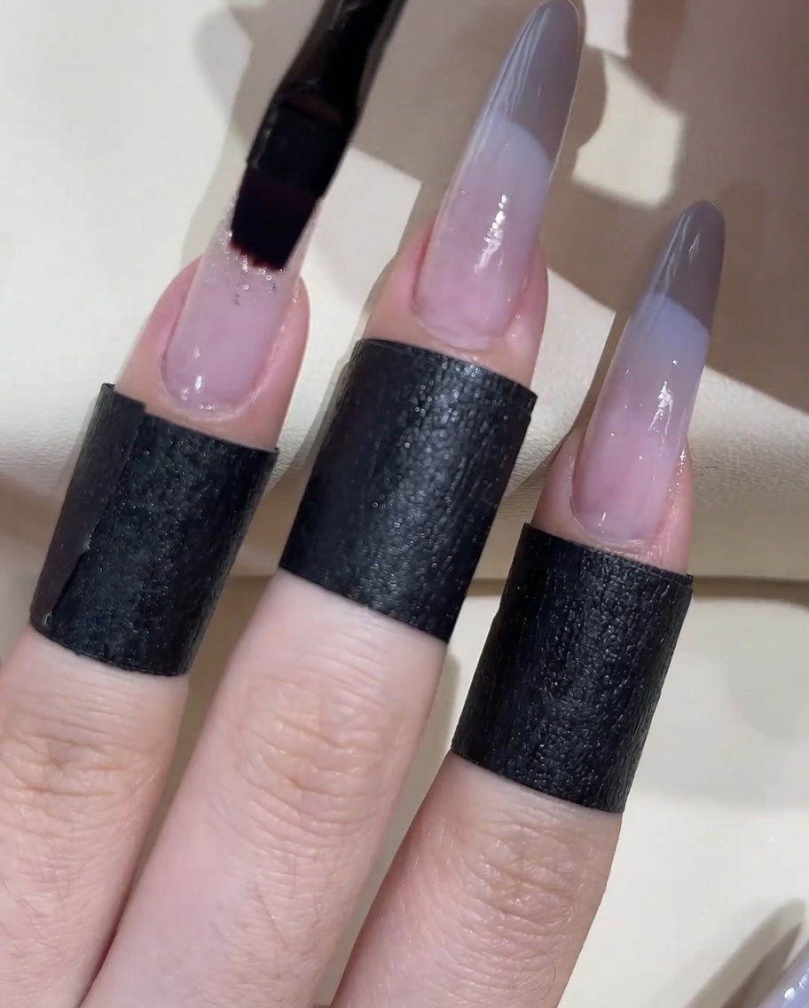 A flat gel brush applying a dollop of thick clear adhesive gel onto a nail surface.