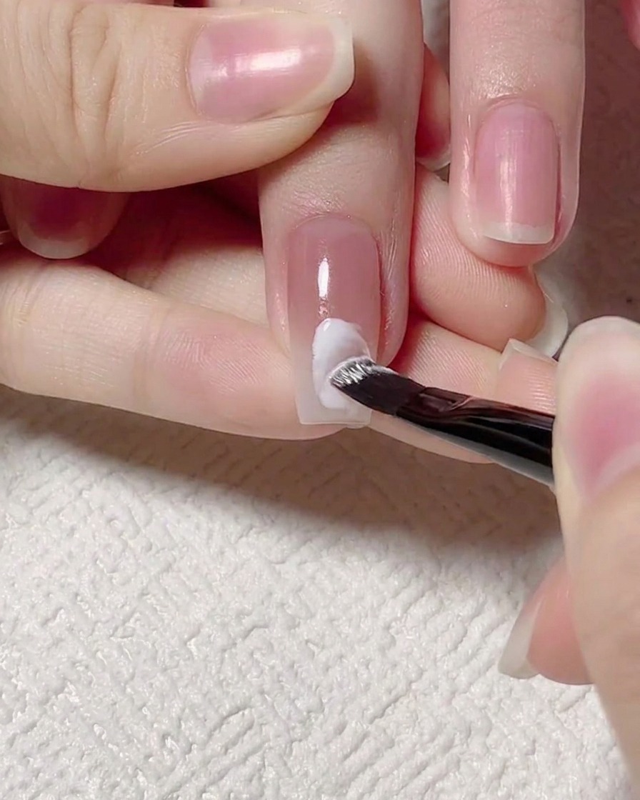 A detail brush painting a white gel wave line across the center of a manicured nail.