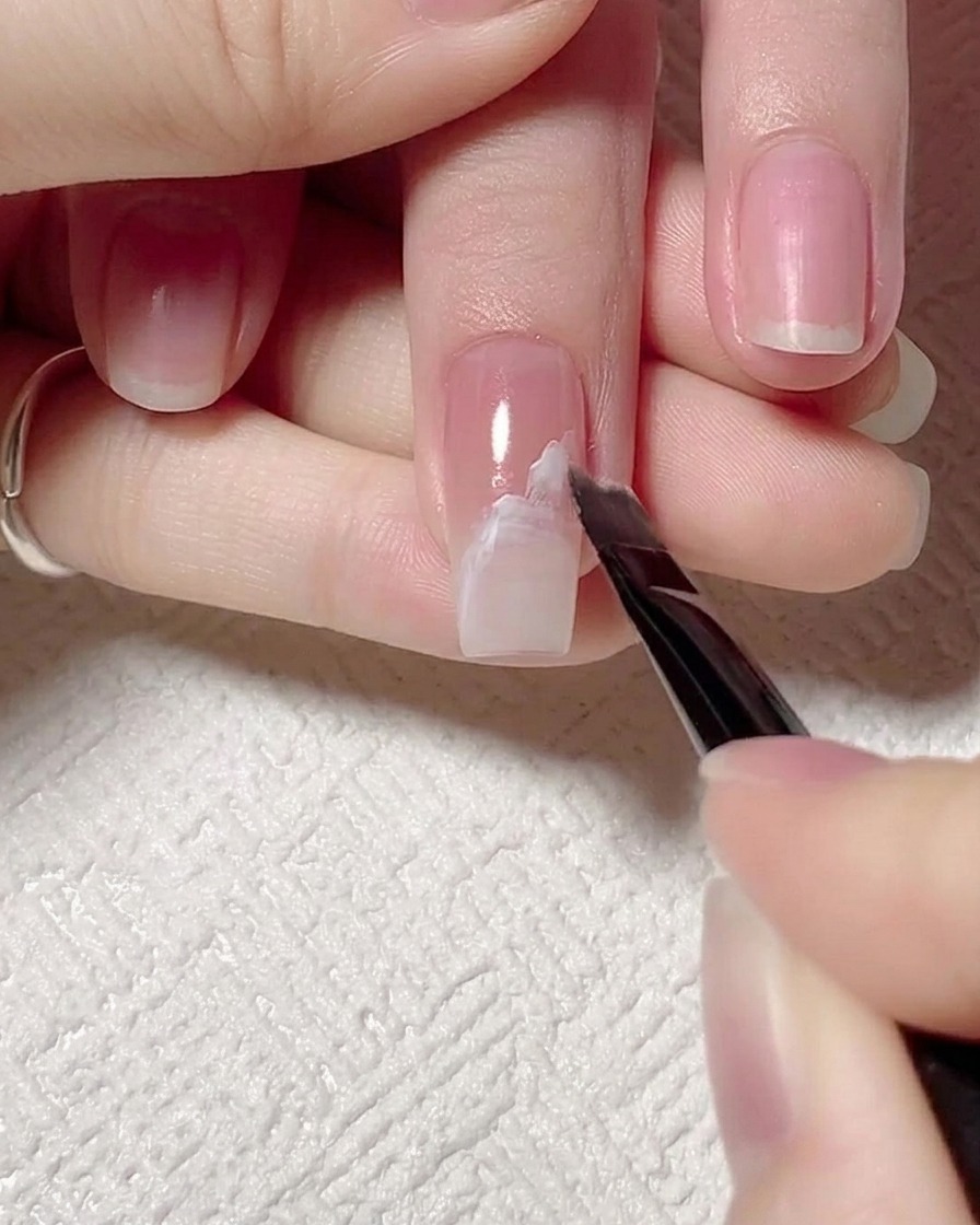 A brush being used to gently blur and diffuse the edges of a white gel wave line on a nail.