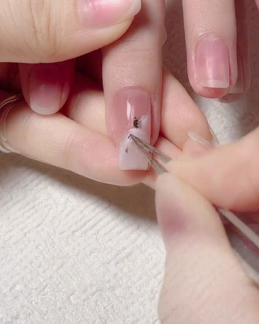 Tweezers holding a small piece of gold foil and placing it onto a nail surface.
