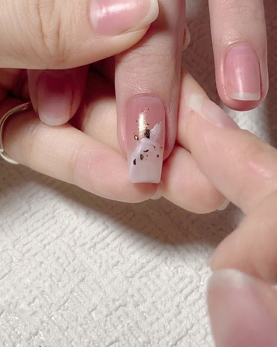 Tweezers being used to press and flatten gold foil flakes onto a nail.