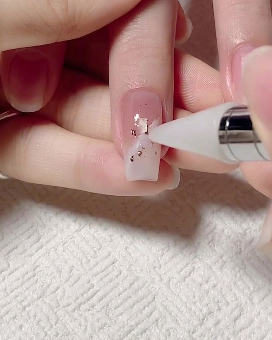 A dotting tool being used to place tiny iridescent shell pieces onto a nail.