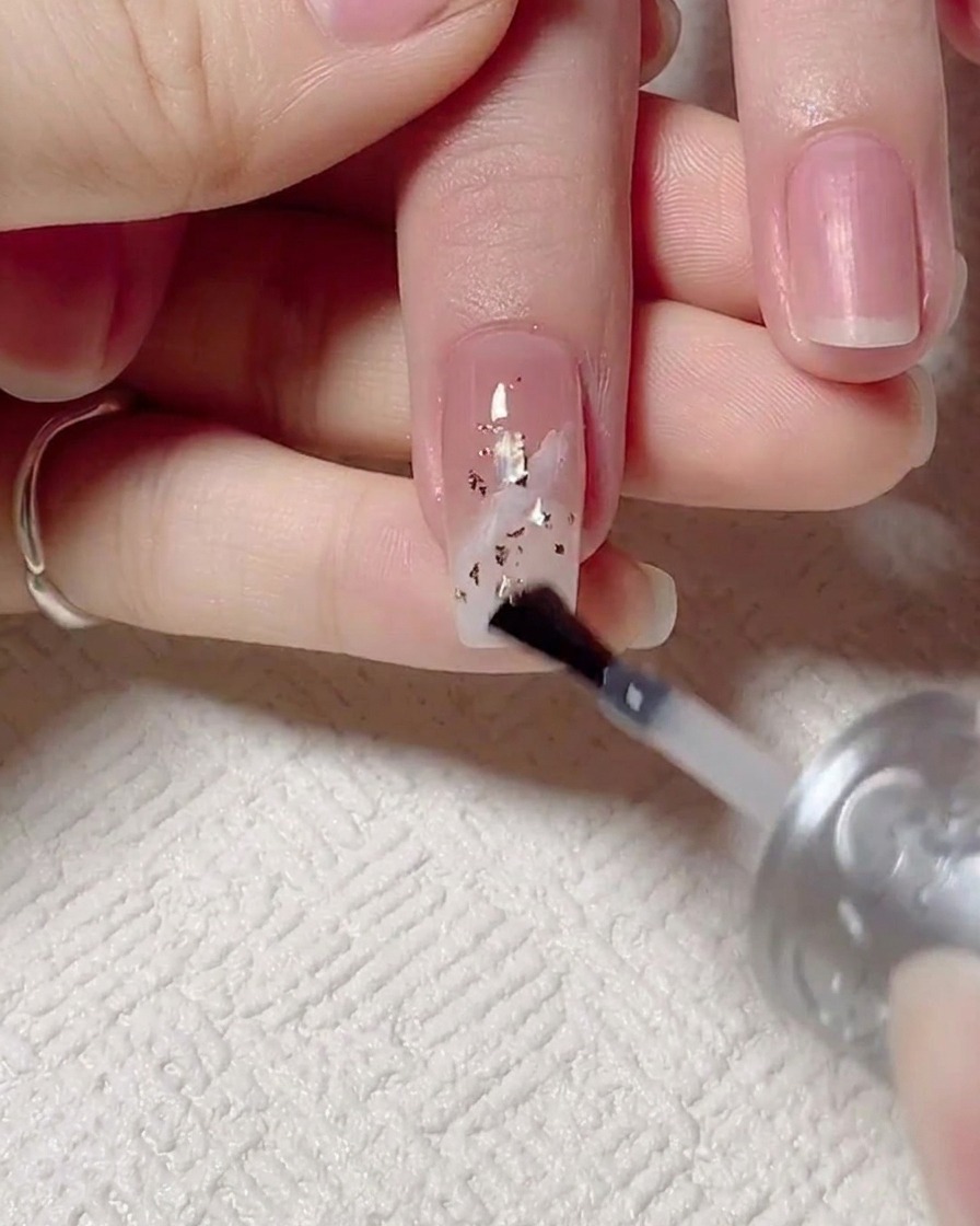 A brush applying a final glossy top coat over the decorated nail, followed by the nail being placed under a UV curing lamp.