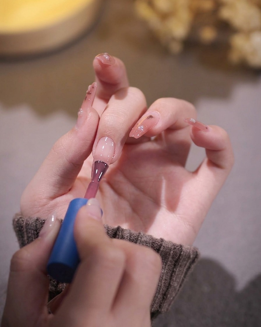 A nail brush applying a coat of translucent pink gel polish onto a prepped nail.