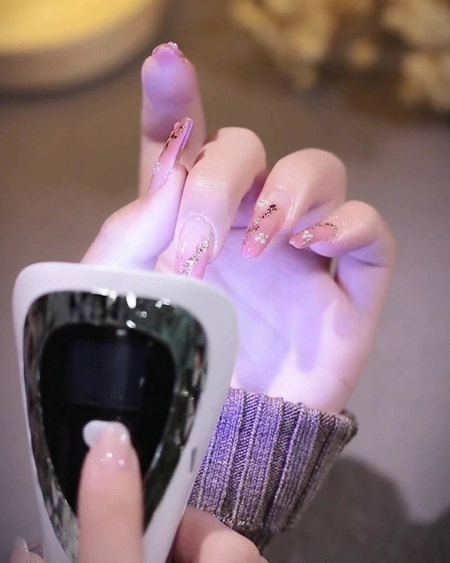A hand with finished nails resting inside a UV nail lamp while the interior glows with purple light.