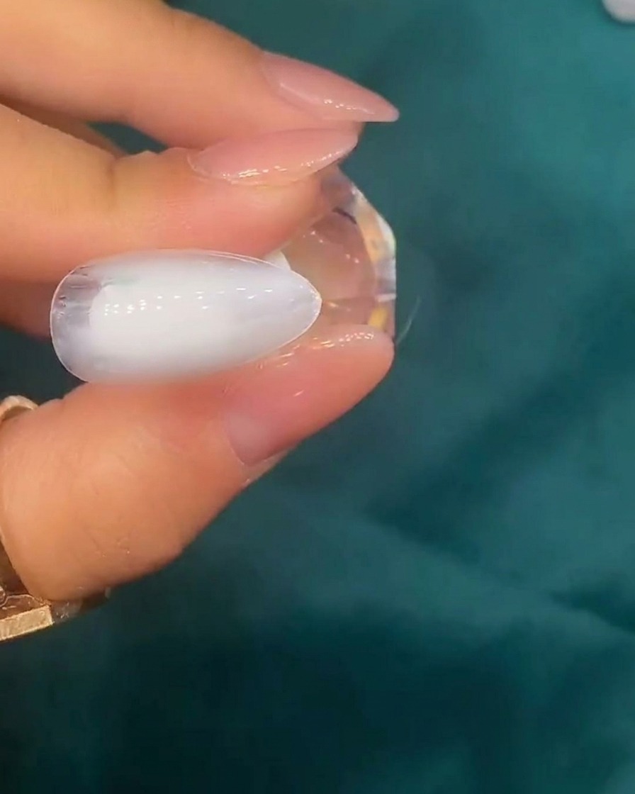 Tweezers placing small iridescent shell pieces onto a nail surface with a white base.