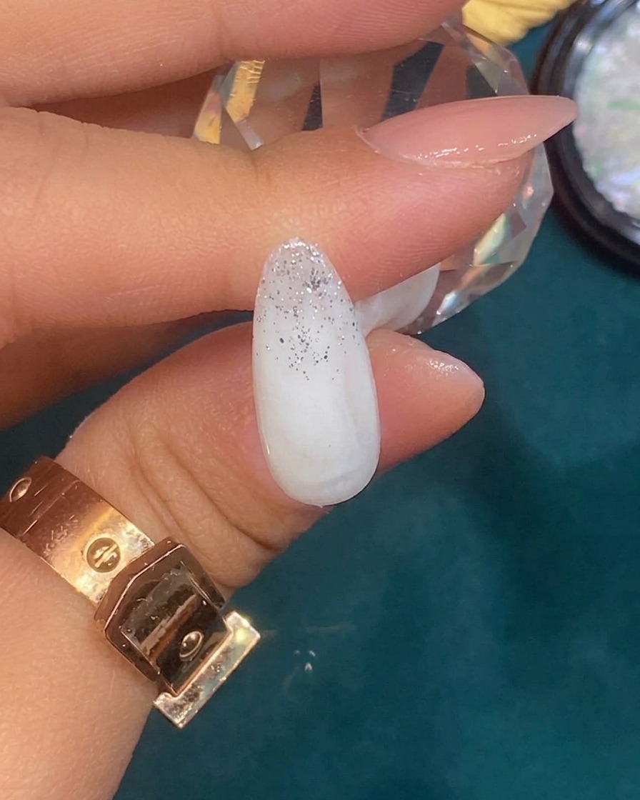 Tweezers placing a small, irregular piece of silver foil onto a nail with a silver glitter gradient.