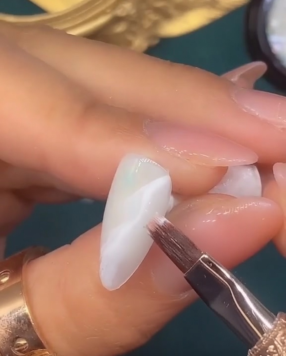 A fine liner brush drawing a thin metallic swirl design over a white blended nail background.