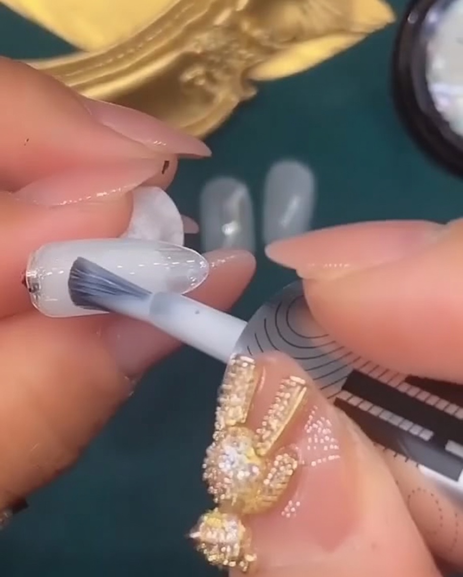 A nail brush applying a coat of translucent white gel polish to the fifth nail.