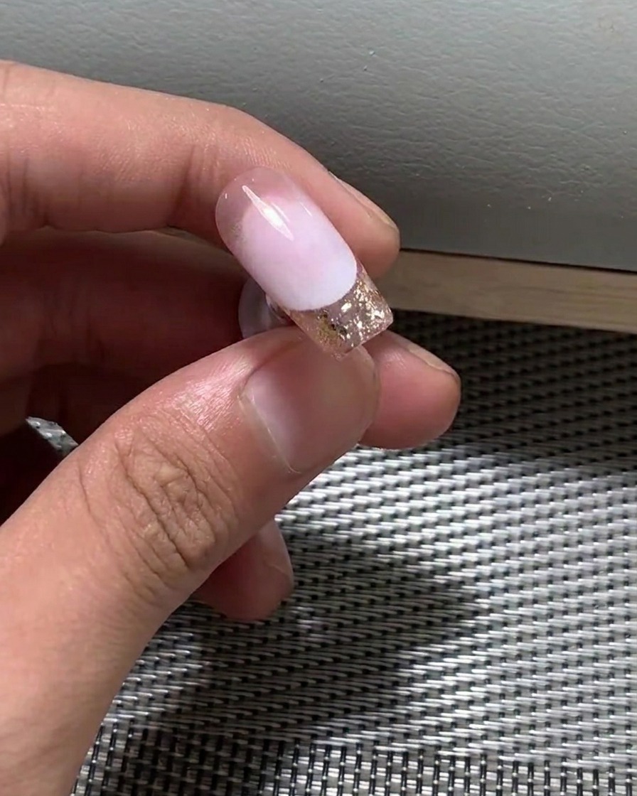 A close-up view of a brush applying a thin layer of nude gel polish onto a nail.