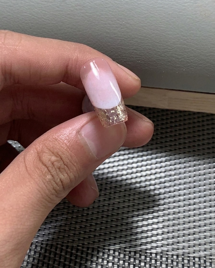 A close-up view of a brush applying a second layer of nude gel polish onto a nail.