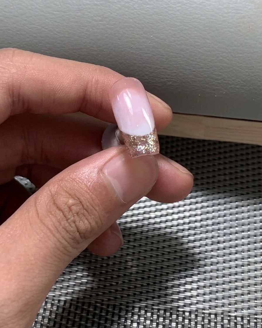 A close-up of fine glitter polish being applied to the free edge of the nail.