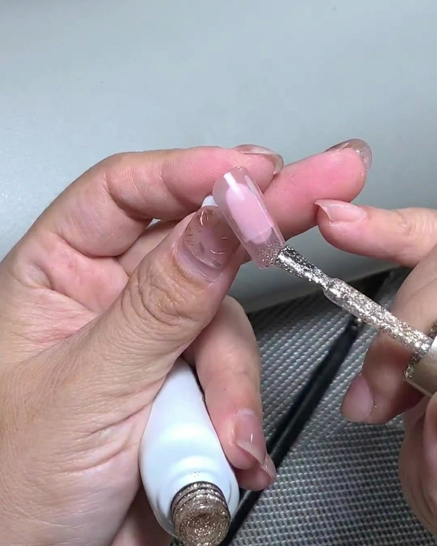 Close-up view of tweezers placing thin flakes of gold foil onto the sparkly glitter nail tip.
