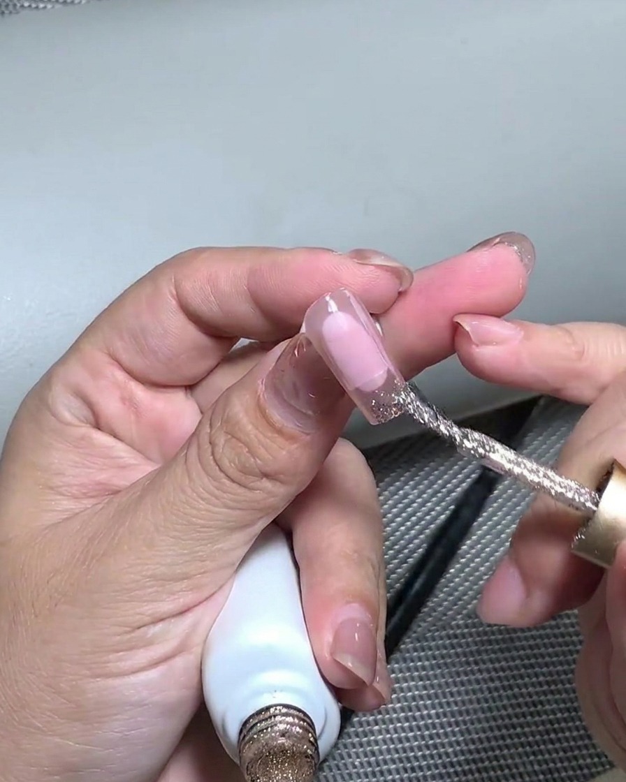 A silicone tool pressing down onto the gold foil applied to the nail tip to flatten it.