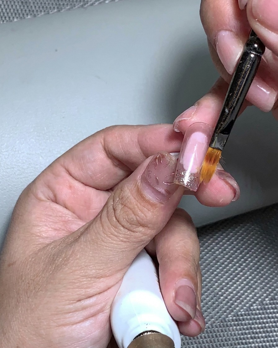 A hand placed inside a UV nail lamp to cure the gold foil application.