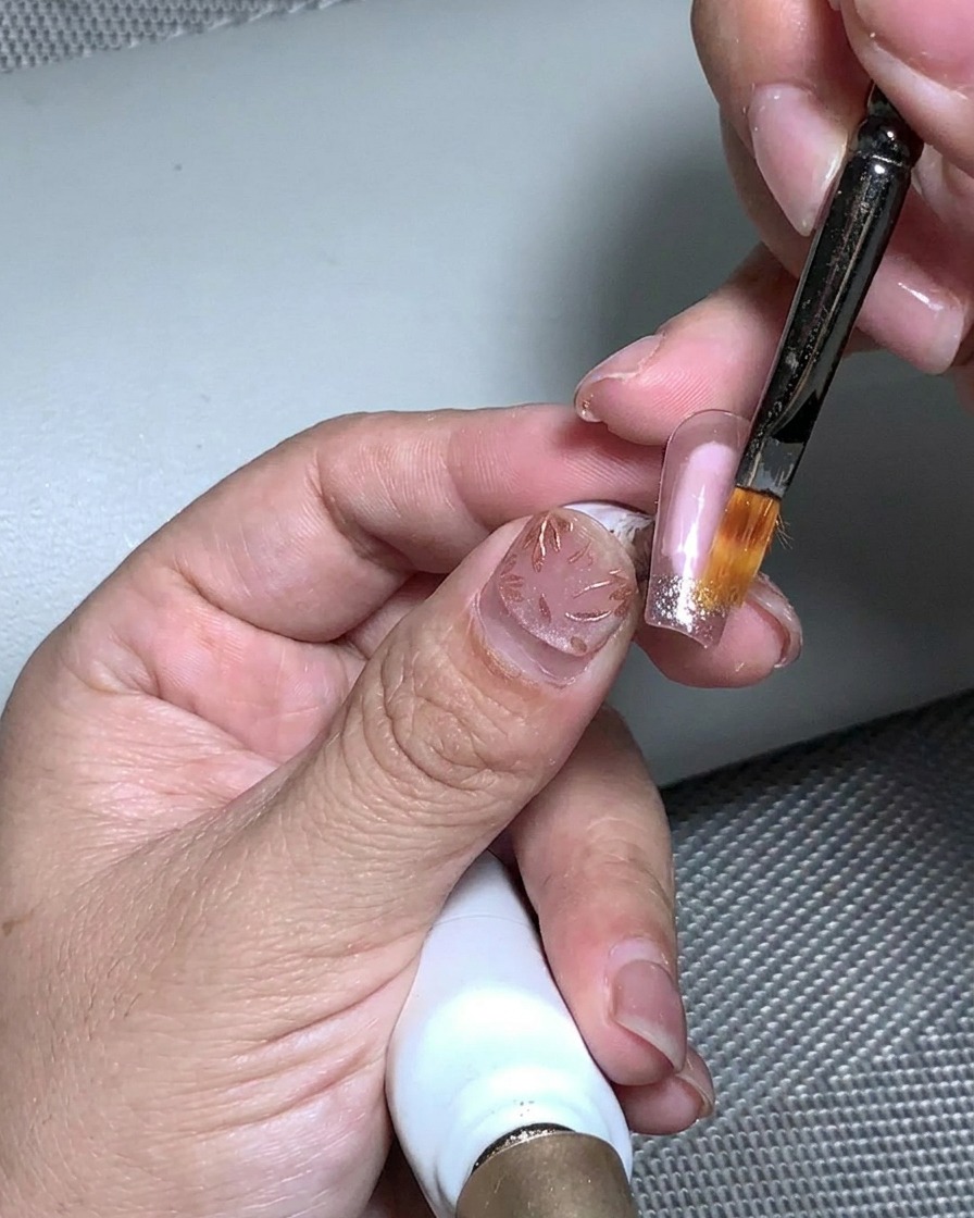 A brush applying clear structural gel over the textured gold foil and glitter surface.