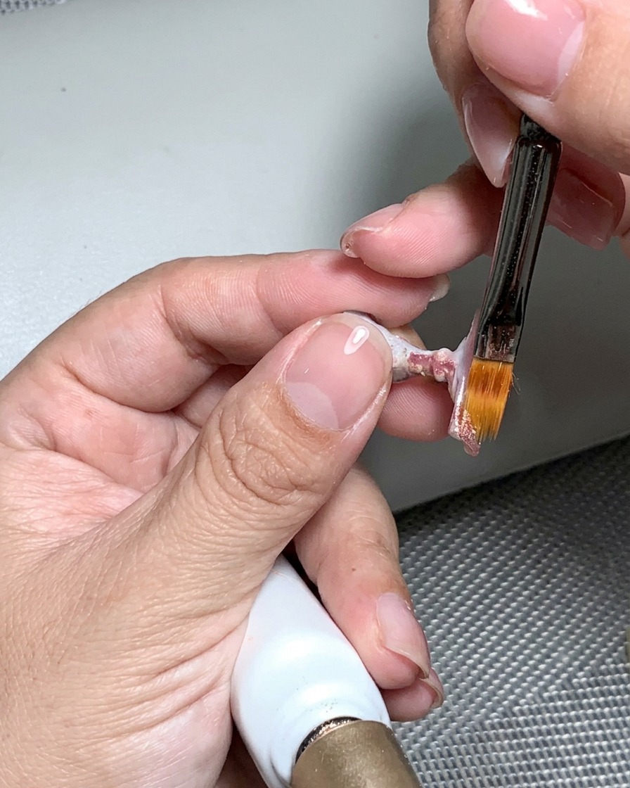 A nail file being used to buff the cured nail surface until it is smooth and even.
