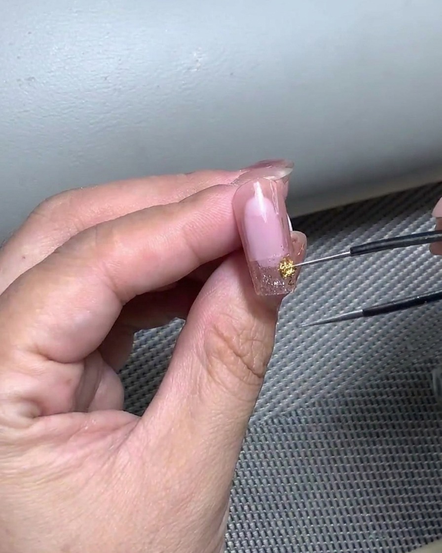 A close-up of a hand using tweezers to delicately place a curved French tip sticker onto a gel-prepared nail.