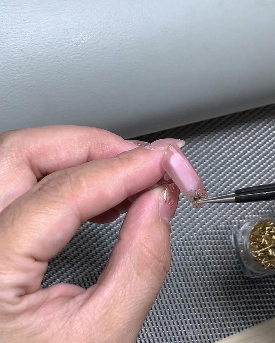 A finger pressing down on a French tip nail sticker to ensure full adhesion to the nail bed.