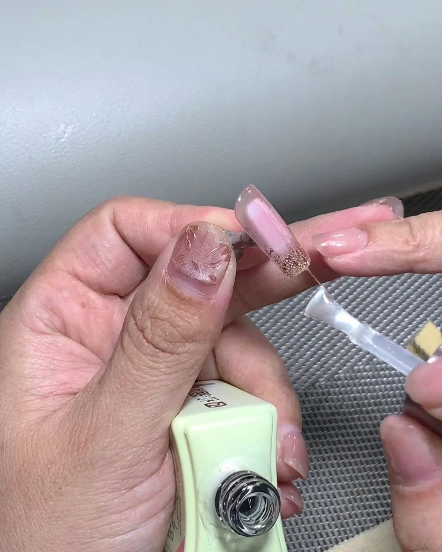 A brush applying a final layer of clear top coat over a completed French tip nail design.