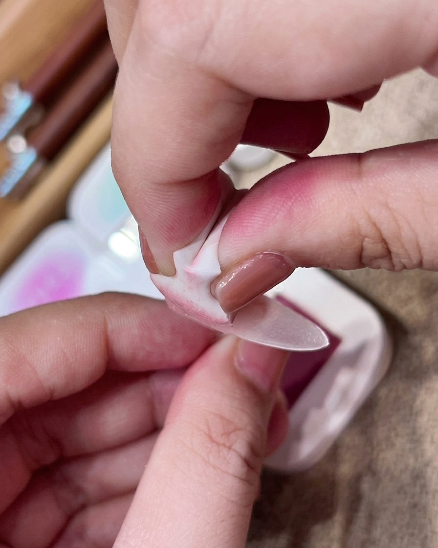 A hand using a small makeup sponge to gently tap pink pigment onto the center of a matte nude nail.