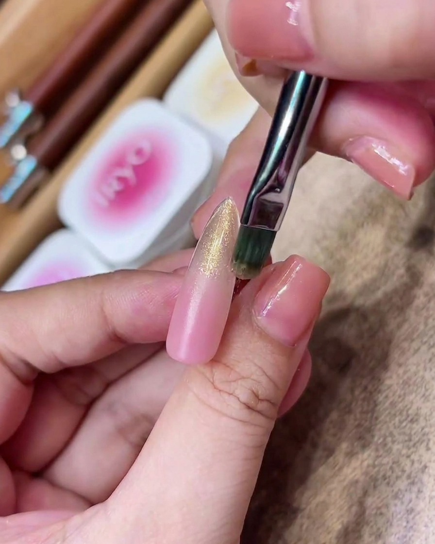 A flat brush applying a streak of sheer gold magnetic gel onto the mid-to-tip section of the nail.